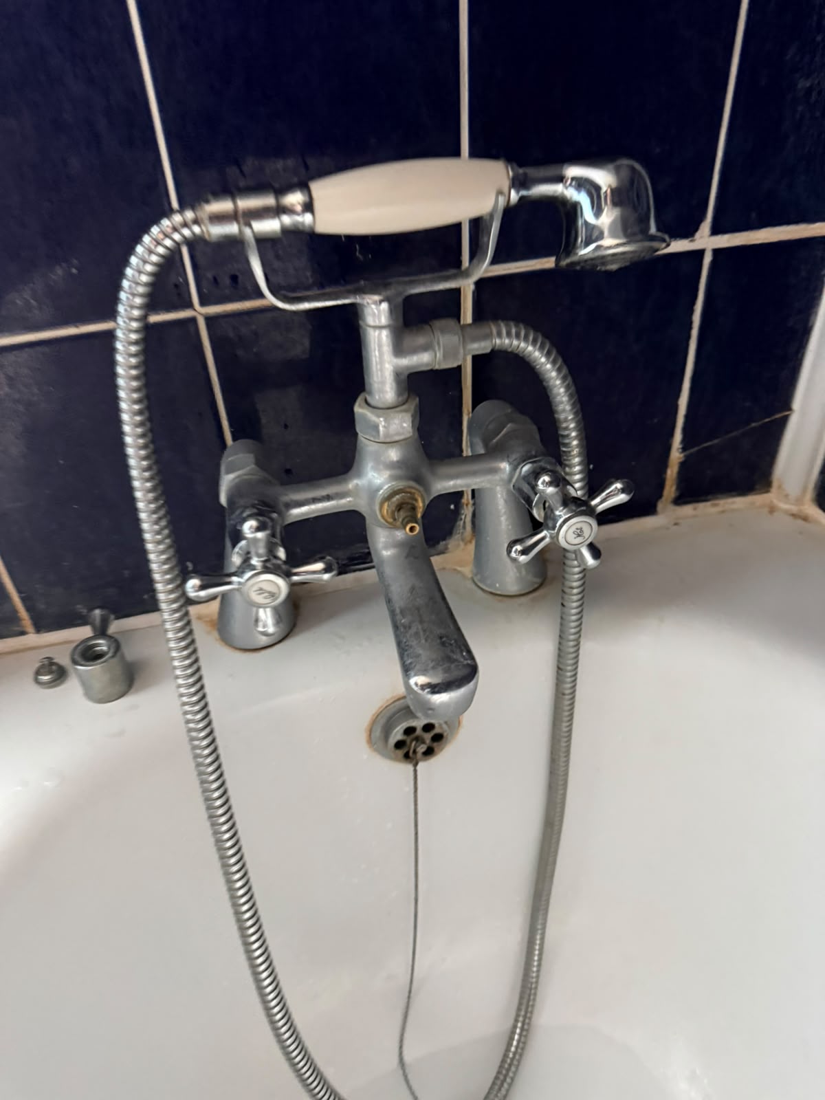 Bath mixer tap with hand shower fitted against navy tiles