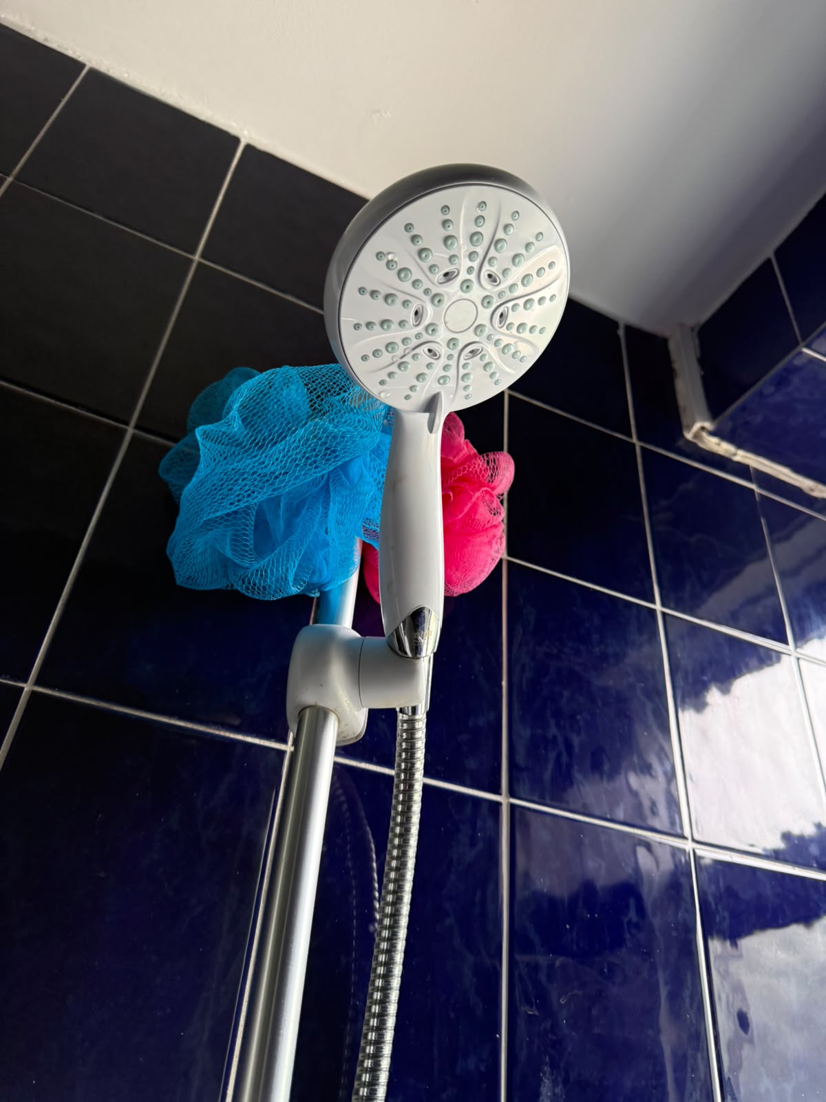 New shower head and hose fitted against navy blue tiles